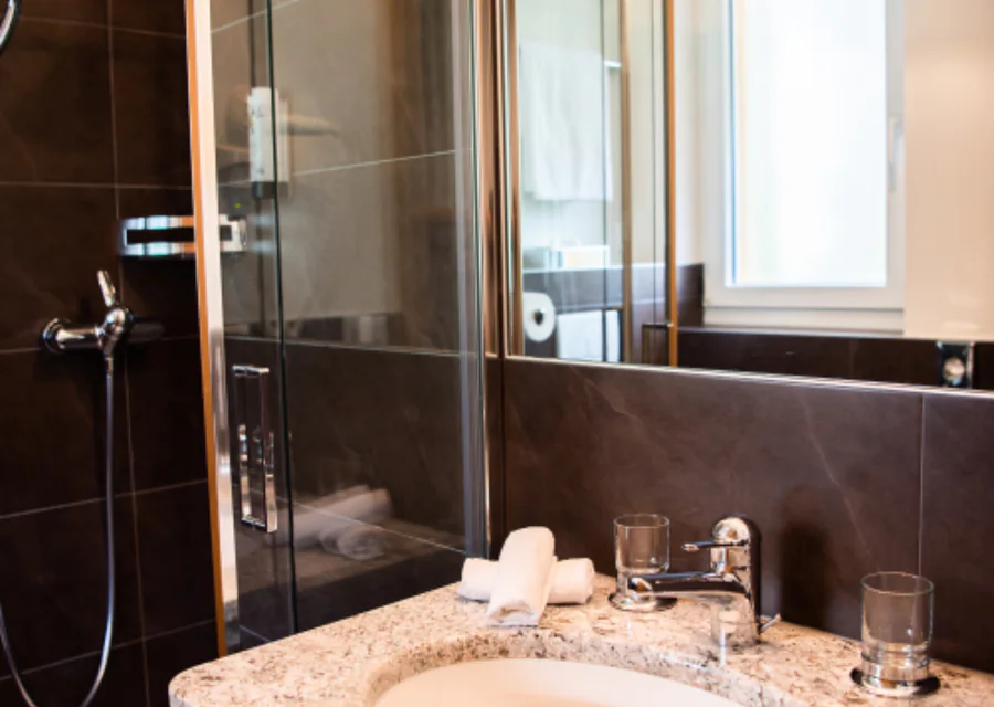 A refitted bathroom with a wall hung basin, a mirror with a lit surround and dark tiled walls.