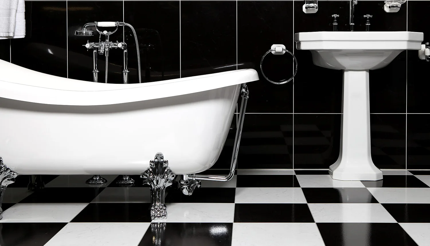 A roll top bath and a pedestal basin, with a black and white tiled floor.