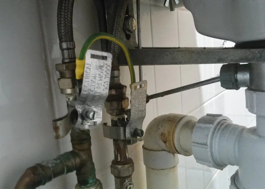 Pipework under a basin, with copper pipe, isolation valves and an earth bonding clamp.