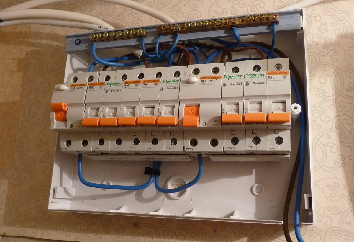 A consumer unit with the cover off, showing a row of circuit breakers and the wiring behind them.