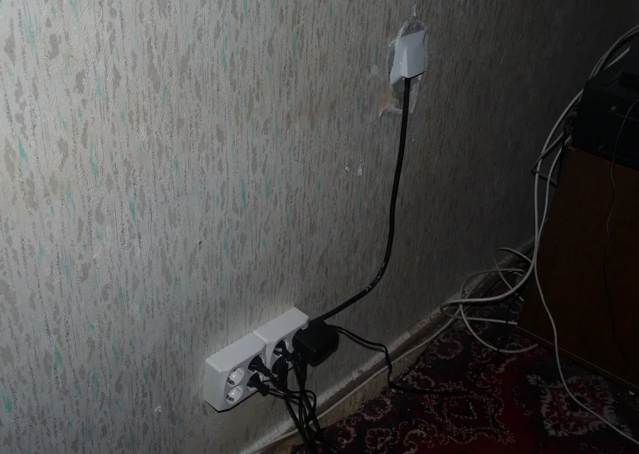 A surface mounted socket on a papered wall with several leads plugged into it.