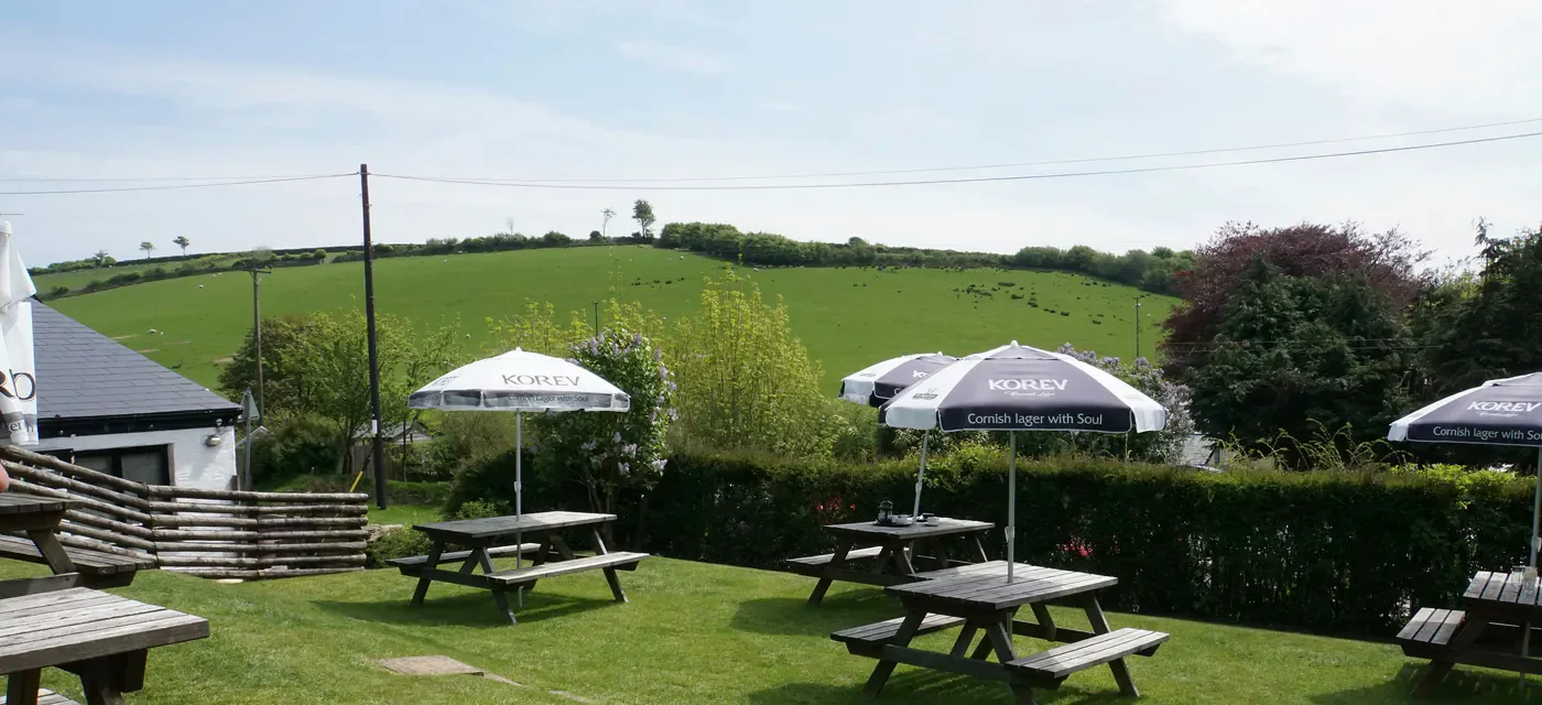 The beer garden: picnic tables and parasols on grass, with fields rising behind.