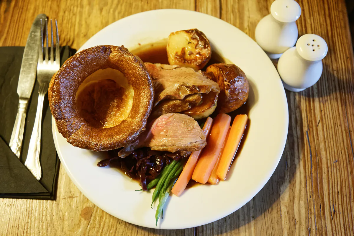 A roast dinner: sliced lamb, a Yorkshire pudding, roast potatoes, carrots and gravy.